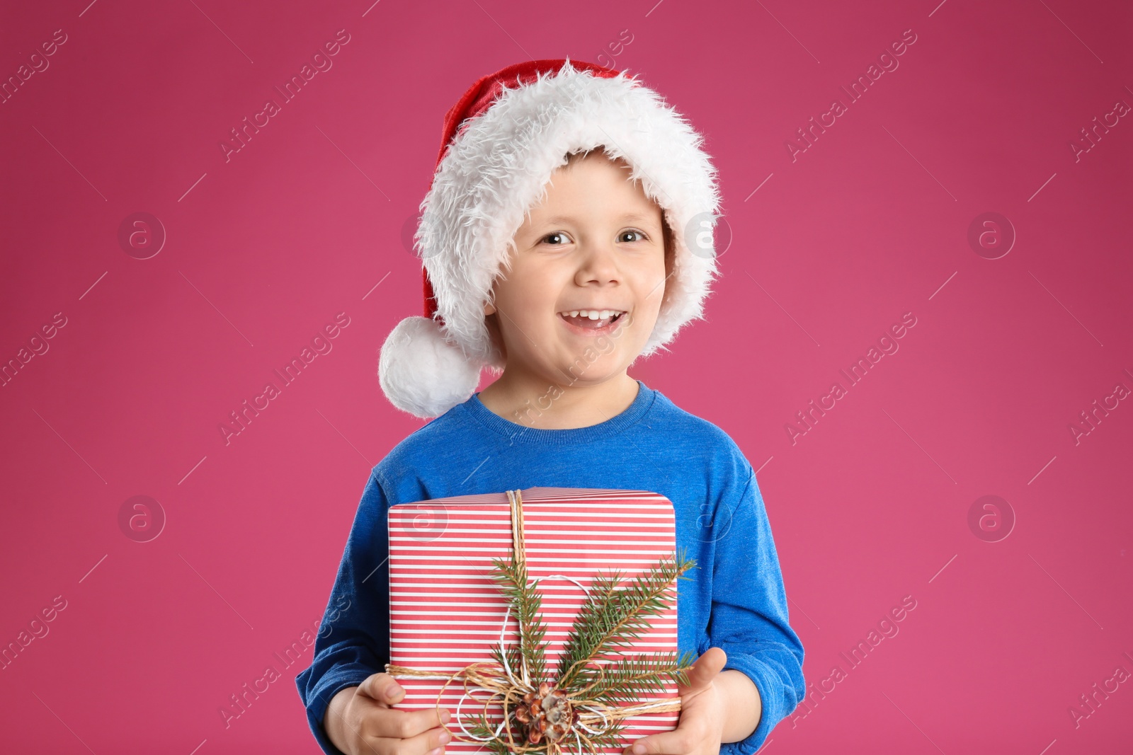 Photo of Cute child in Santa hat with Christmas gift on pink background