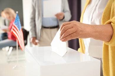 Elderly woman putting ballot paper into box at polling station, closeup