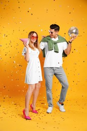 Photo of Happy couple with disco ball and confetti on yellow background