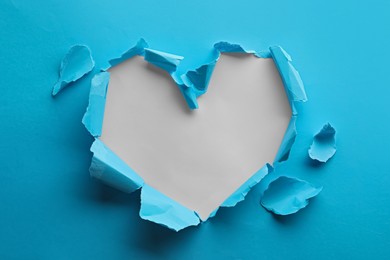 Torn heart shaped hole in light blue paper on white background
