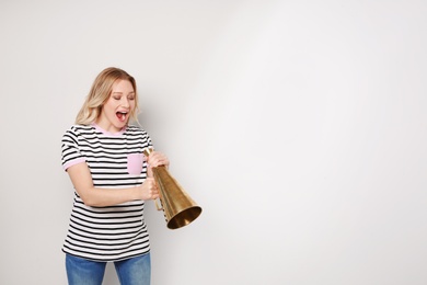 Young woman shouting into megaphone on light background. Space for text