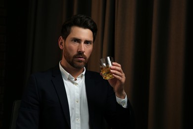 Photo of Man in suit holding glass of whiskey with ice cubes on brown background