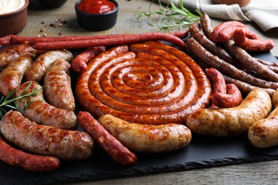 Different delicious sausages with rosemary and sauces on wooden table, closeup. Assortment of beer snacks