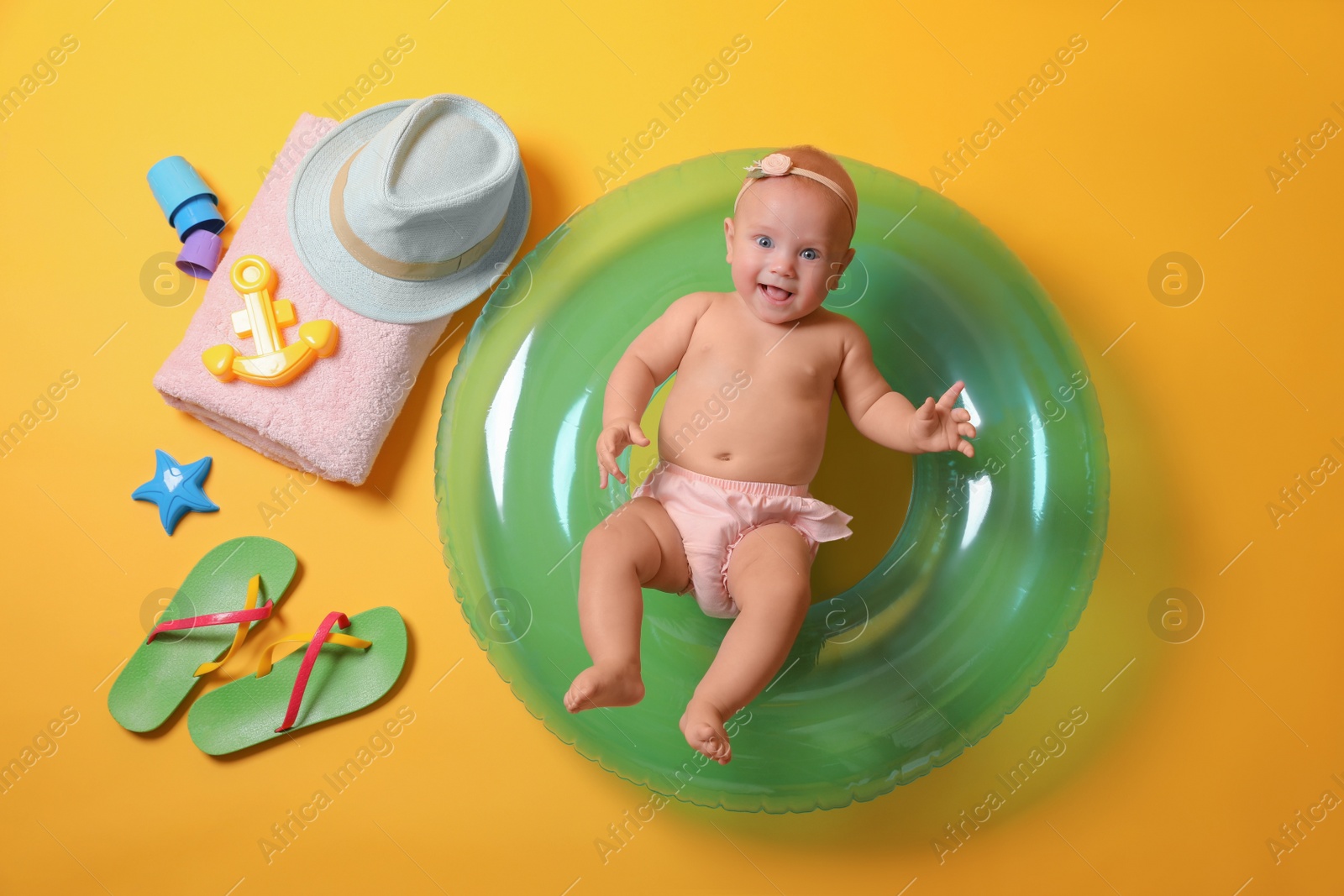 Photo of Cute little baby with inflatable ring and beach accessories on yellow background, top view