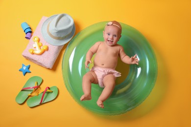 Cute little baby with inflatable ring and beach accessories on yellow background, top view