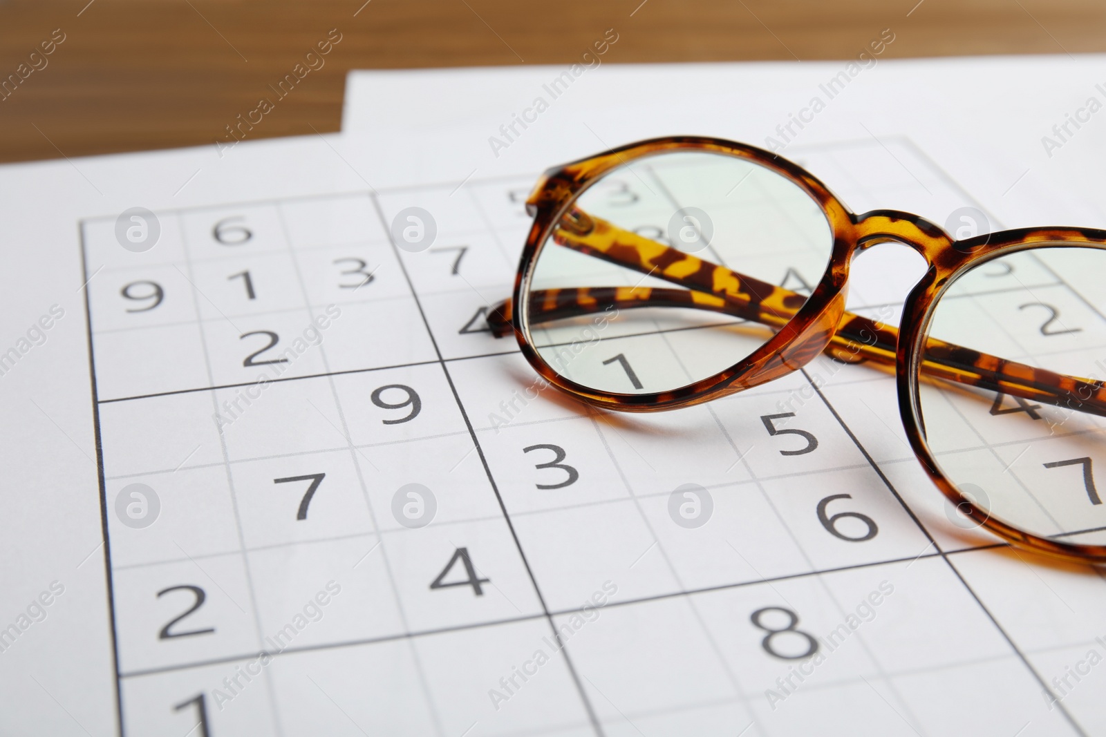 Photo of Sudoku and eyeglasses on wooden table, closeup