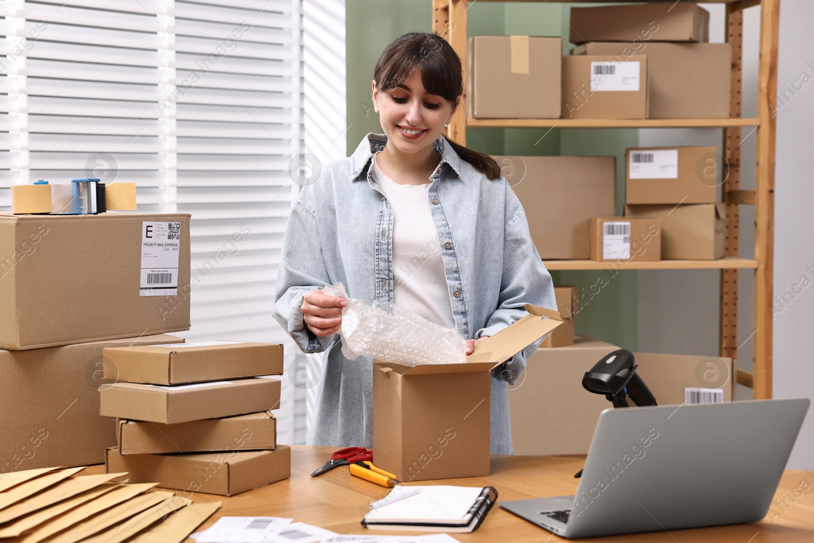 Photo of Post office worker packing parcel at wooden table indoors