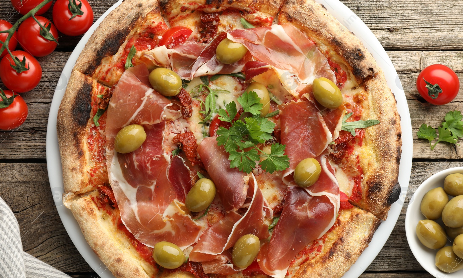 Photo of Tasty pizza with cured ham, olives, tomatoes and parsley on wooden table, top view