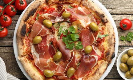 Photo of Tasty pizza with cured ham, olives, tomatoes and parsley on wooden table, top view