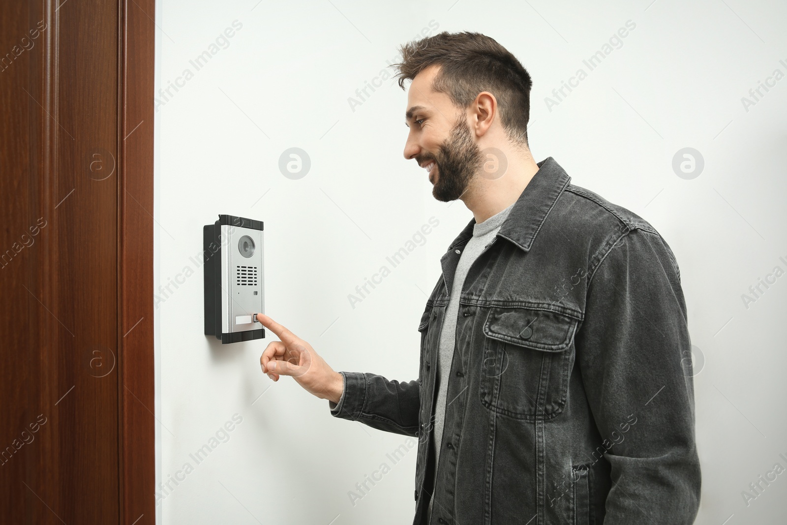 Photo of Happy man ringing intercom with camera in entryway