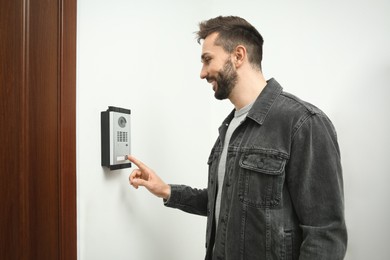 Photo of Happy man ringing intercom with camera in entryway