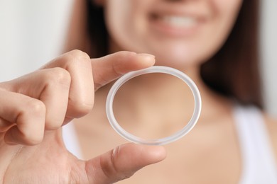 Woman holding diaphragm vaginal contraceptive ring on blurred background, closeup