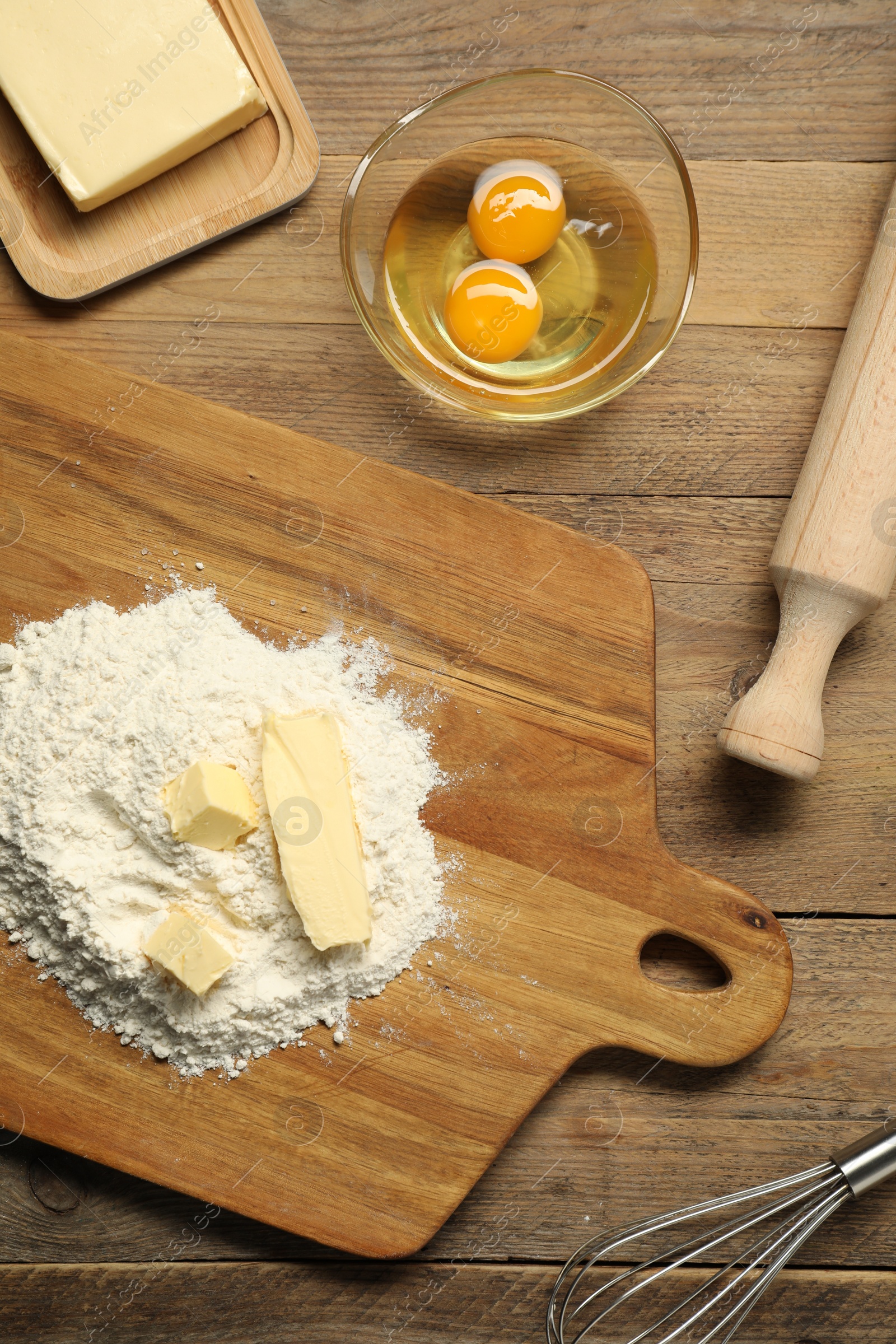 Photo of Board with fresh butter and flour on wooden table, flat lay