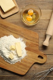 Photo of Board with fresh butter and flour on wooden table, flat lay