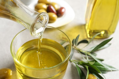 Photo of Pouring fresh olive oil into glass on table