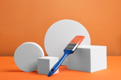 Photo of Scene with podium for product presentation. Figures of different geometric shapes and paint brush on orange background