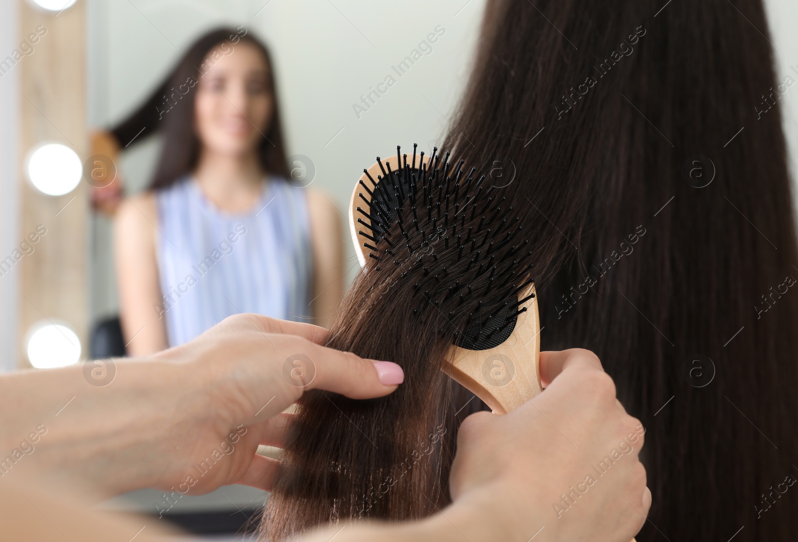 Photo of Woman combing friend's hair with cushion brush indoors, closeup