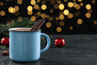 Delicious hot chocolate with cocoa sticks near Christmas decor on black table against blurred lights, closeup. Space for text