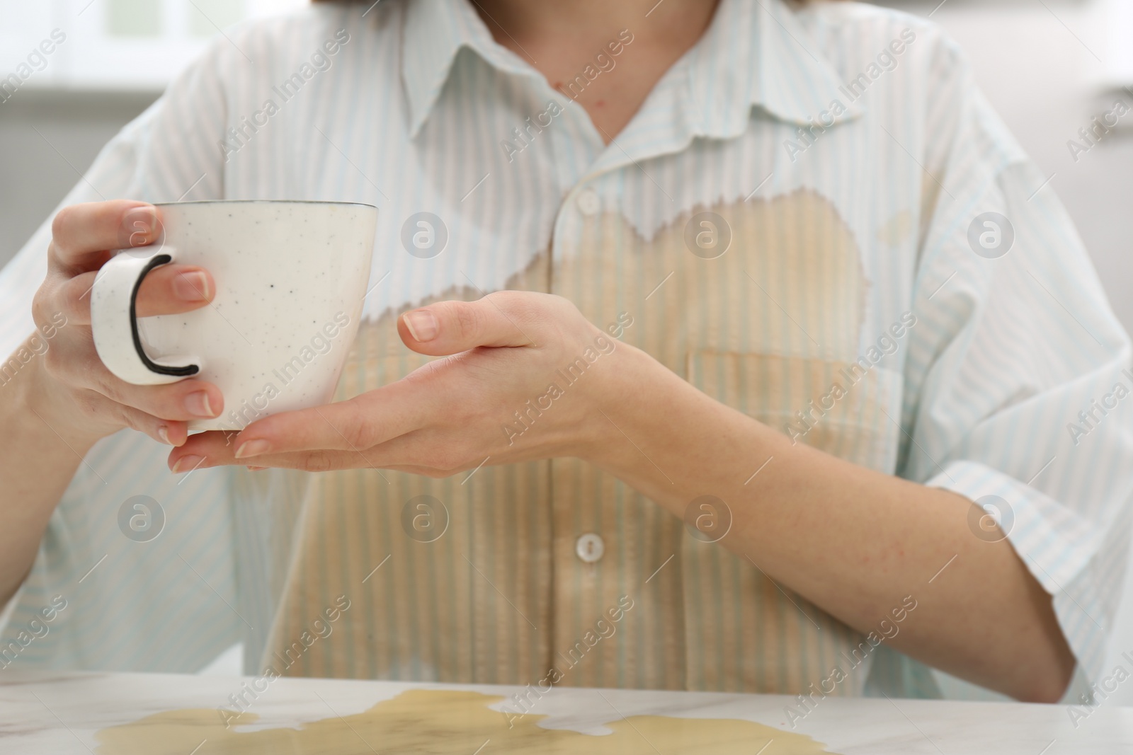 Photo of Woman with spilled coffee over her shirt at marble table indoors, closeup