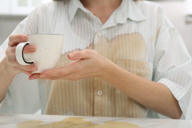 Photo of Woman with spilled coffee over her shirt at marble table indoors, closeup