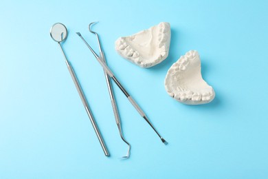 Photo of Dental model with gums and dentist tools on light blue background, flat lay. Cast of teeth