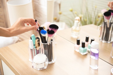 Photo of Woman taking brush from organizer for makeup cosmetic products on table
