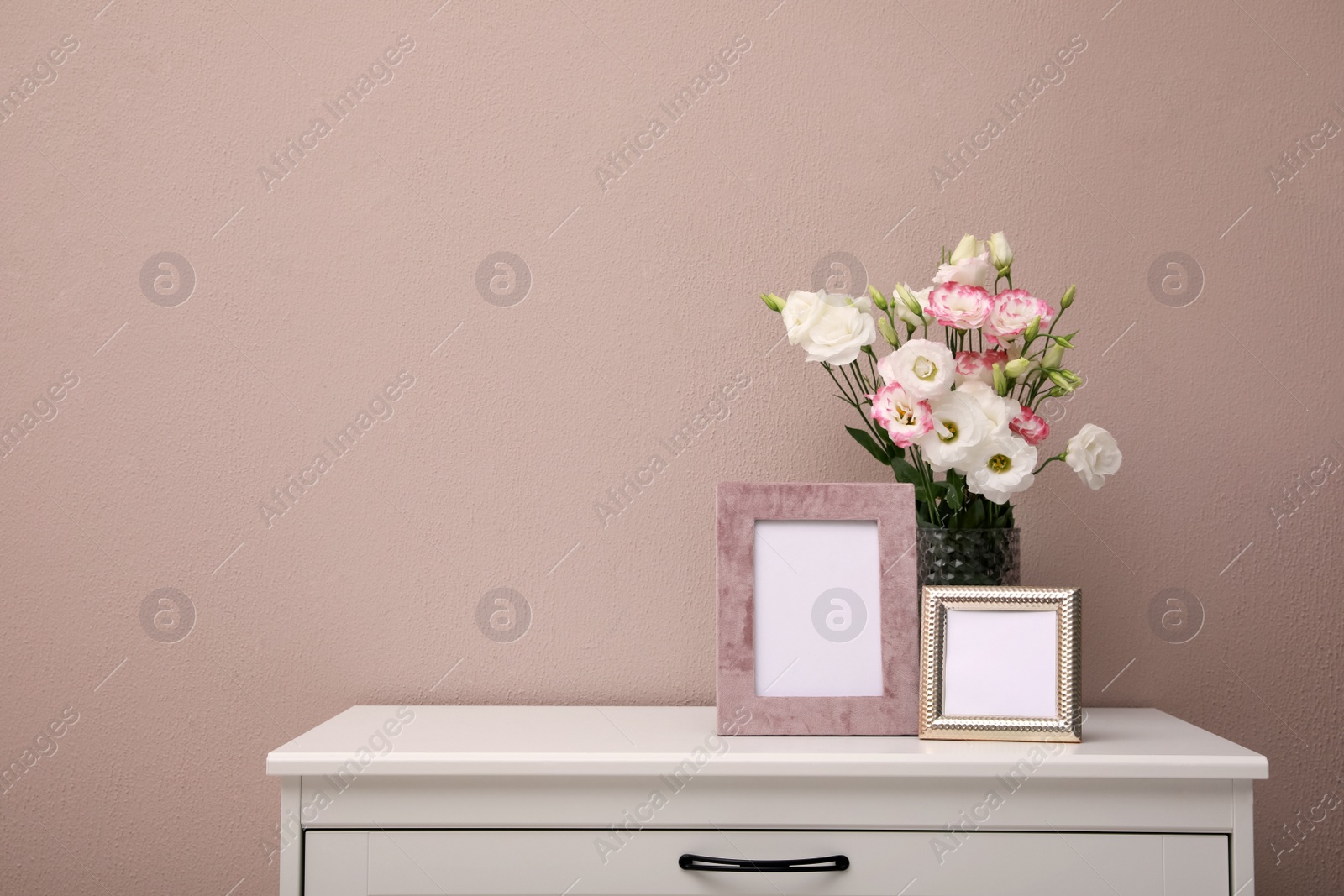 Photo of Empty photo frames and beautiful bouquet on white chest of drawers near pink wall, space for text