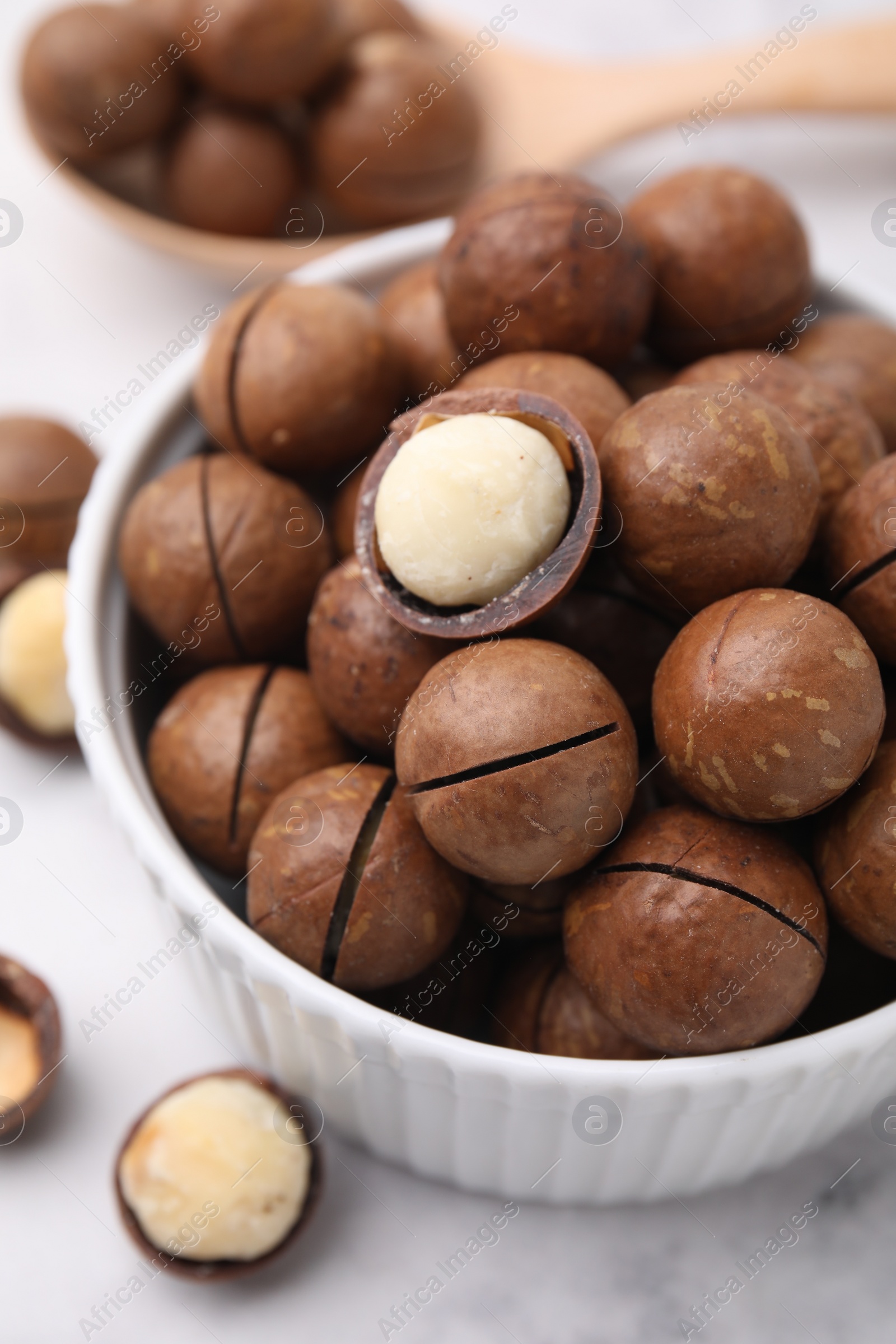 Photo of Tasty Macadamia nuts in bowl on white table, closeup