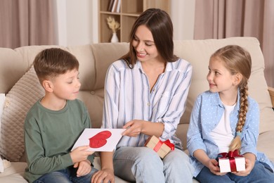 Cute little children presenting their mother with gifts on sofa at home
