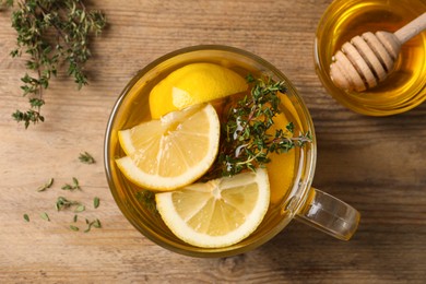 Photo of Fresh thyme tea with pieces of lemon and honey on wooden table, flat lay