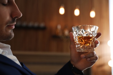 Photo of Young man with glass of whiskey indoors, closeup