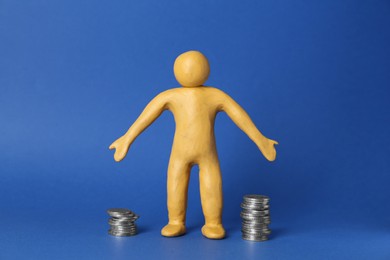 Photo of Human figure made of yellow plasticine with stacked coins on blue background