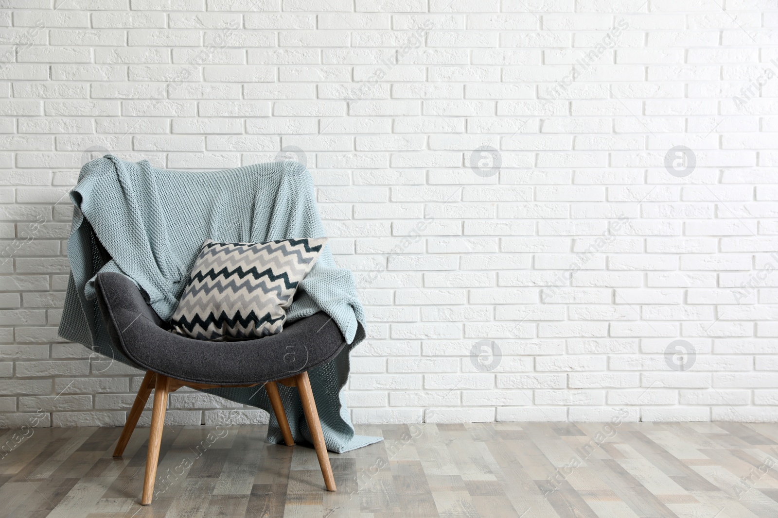 Photo of Cozy armchair with plaid and pillow near brick wall, space for text. Stylish interior design