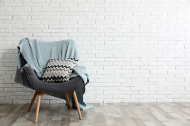 Photo of Cozy armchair with plaid and pillow near brick wall, space for text. Stylish interior design