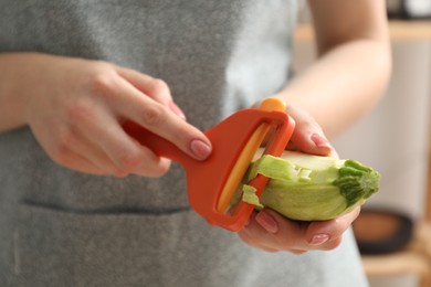 Photo of Woman peeling fresh zucchini with peeler, closeup