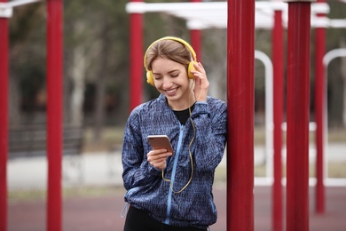 Photo of Young woman with headphones listening to music on sports ground