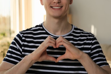 Photo of Happy volunteer making heart with his hands in room, closeup