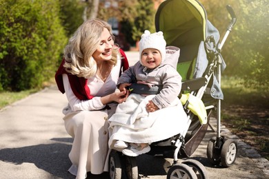 Photo of Happy mother with her daughter in stroller outdoors on sunny day