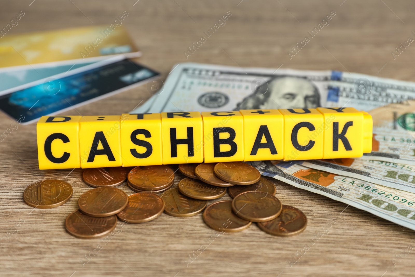 Photo of Yellow cubes with word Cashback, money and credit cards on wooden table, closeup