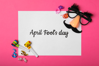 Photo of Paper note with phrase APRIL FOOL'S DAY and decor on pink background, flat lay