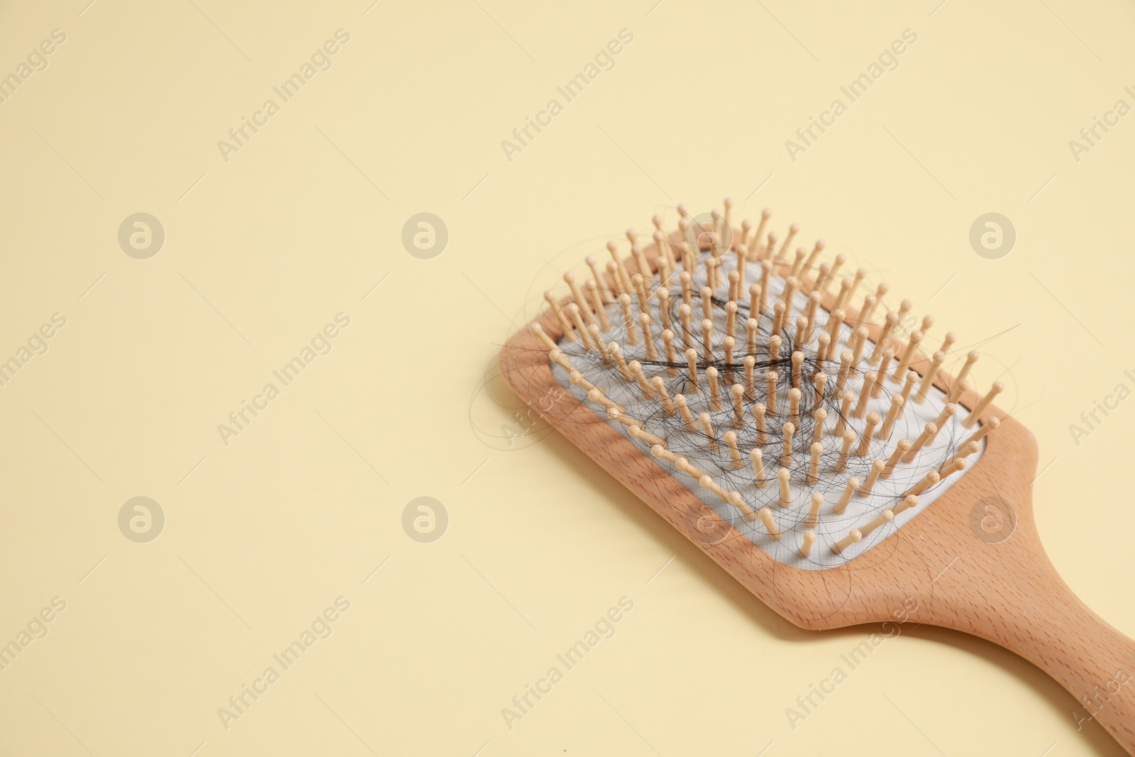 Photo of Wooden brush with lost hair on beige background, closeup. Space for text