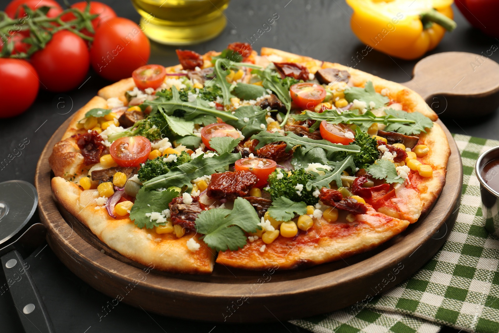 Photo of Delicious vegetarian pizza, ingredients and cutter on black table, closeup