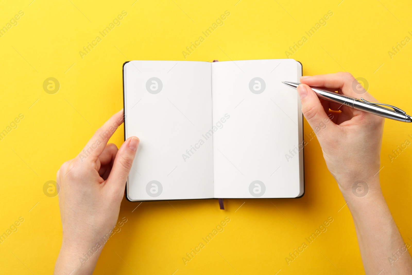 Photo of Woman writing in notebook on yellow background, top view