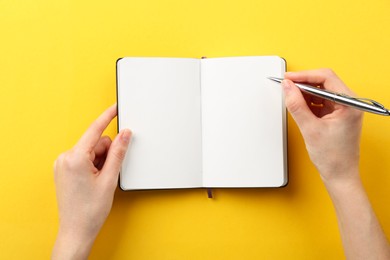 Photo of Woman writing in notebook on yellow background, top view