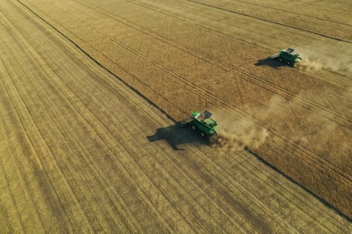 Beautiful aerial view of modern combine harvesters working in field on sunny day. Agriculture industry