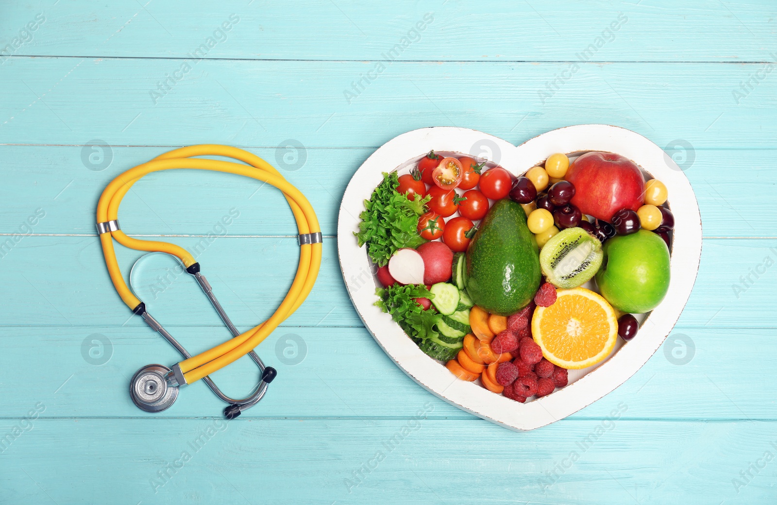 Photo of Heart shaped plate with fresh fruits, vegetables and stethoscope on wooden background, top view. Cardiac diet