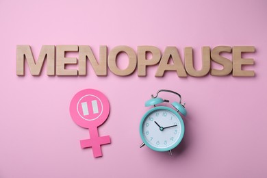 Photo of Word Menopause made of wooden letters, female gender sign and alarm clock on pink background, flat lay