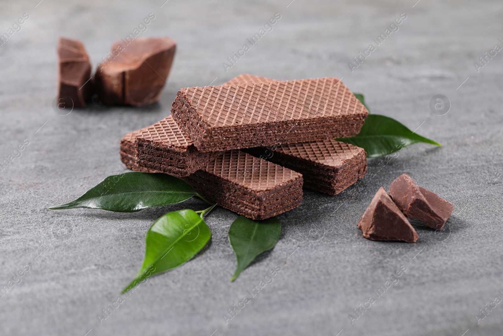 Photo of Delicious chocolate wafers with leaves on grey stone background