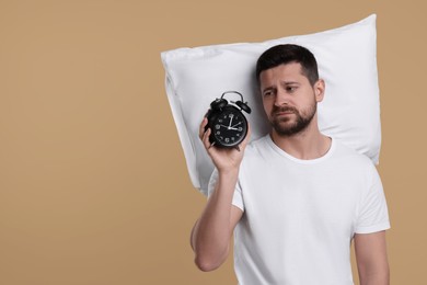 Photo of Sleepy man with pillow and alarm clock on beige background, space for text. Insomnia problem