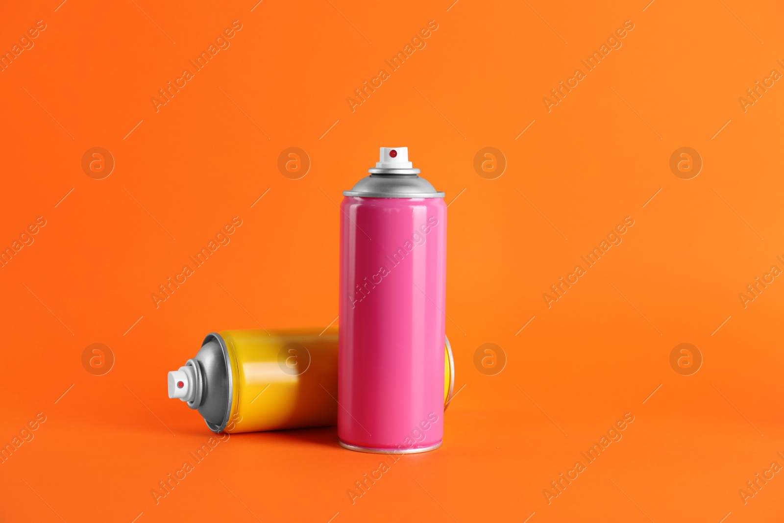 Photo of Colorful cans of spray paints on orange background. Space for text